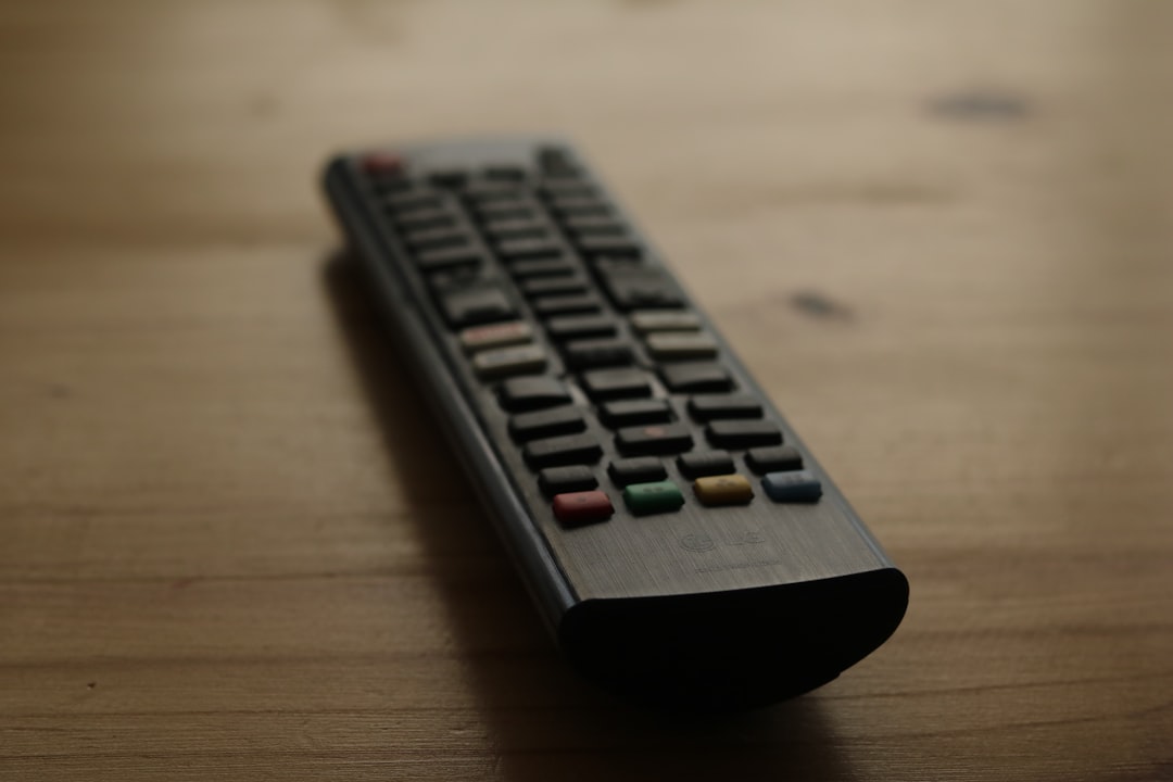 A black remote control rests on a wooden surface.